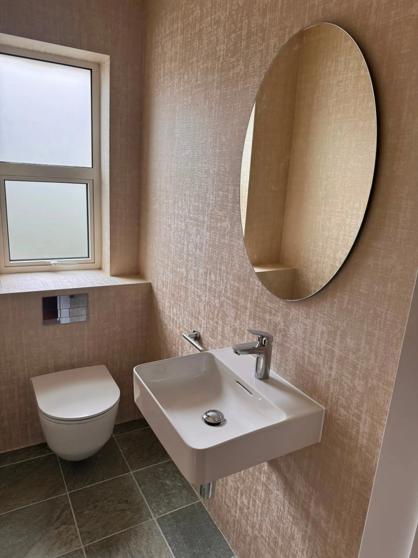 Blush pink cloakroom with oval mirror, wall-hung basin and slate floor tiling by Heat Solution London