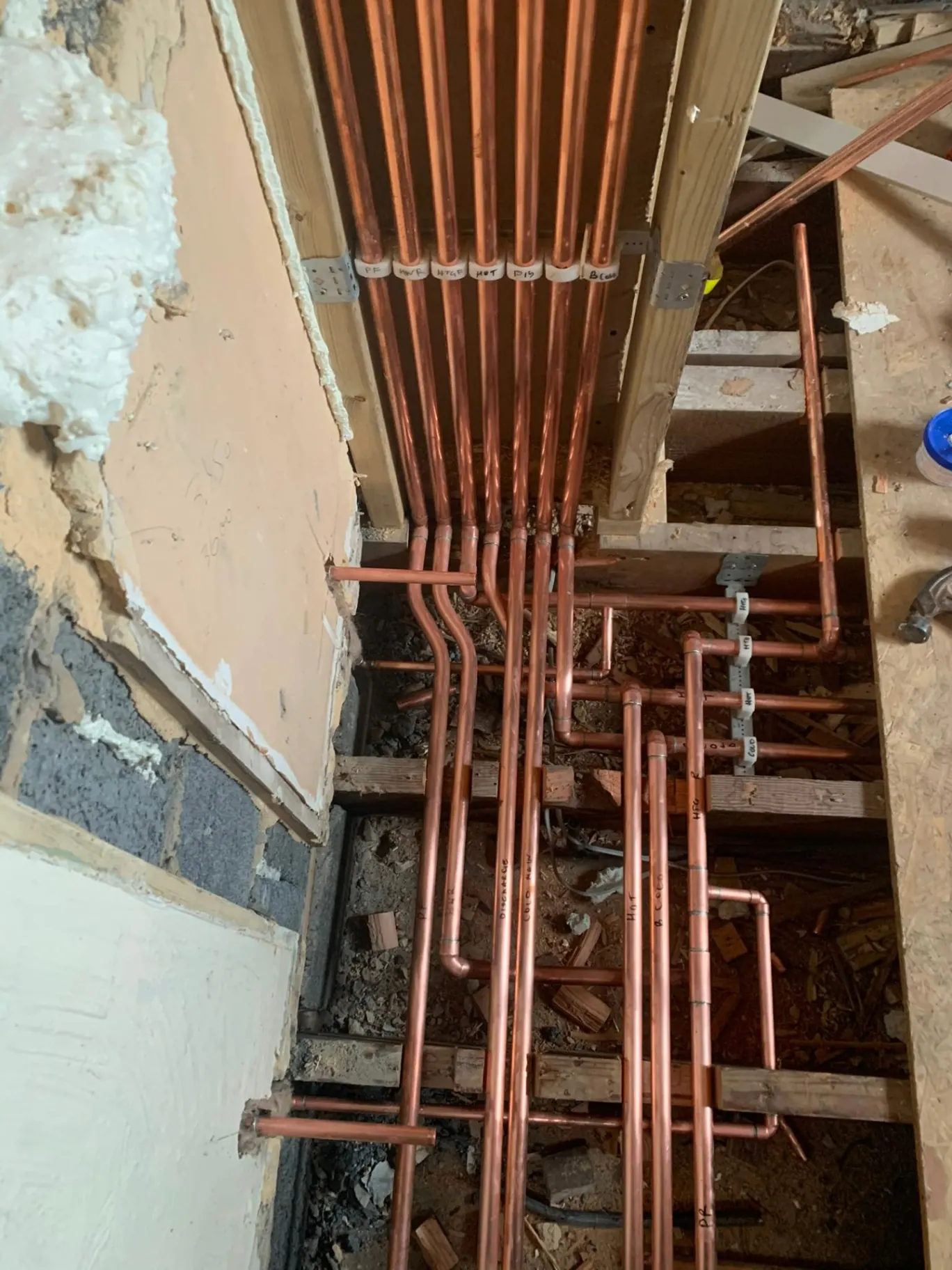 Neat labelled copper plumbing pipework under a bathroom floor, installed by Heat Solution London in Ashford, Surrey