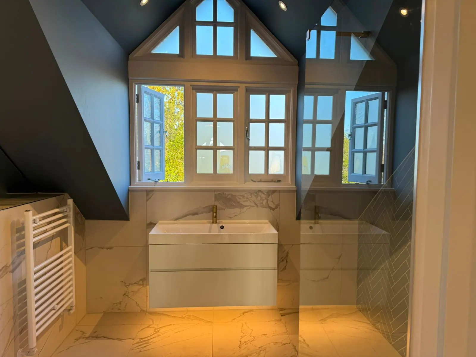 Loft bathroom with dark blue vaulted ceiling, wall-hung vanity and marble-effect tiling by Heat Solution London