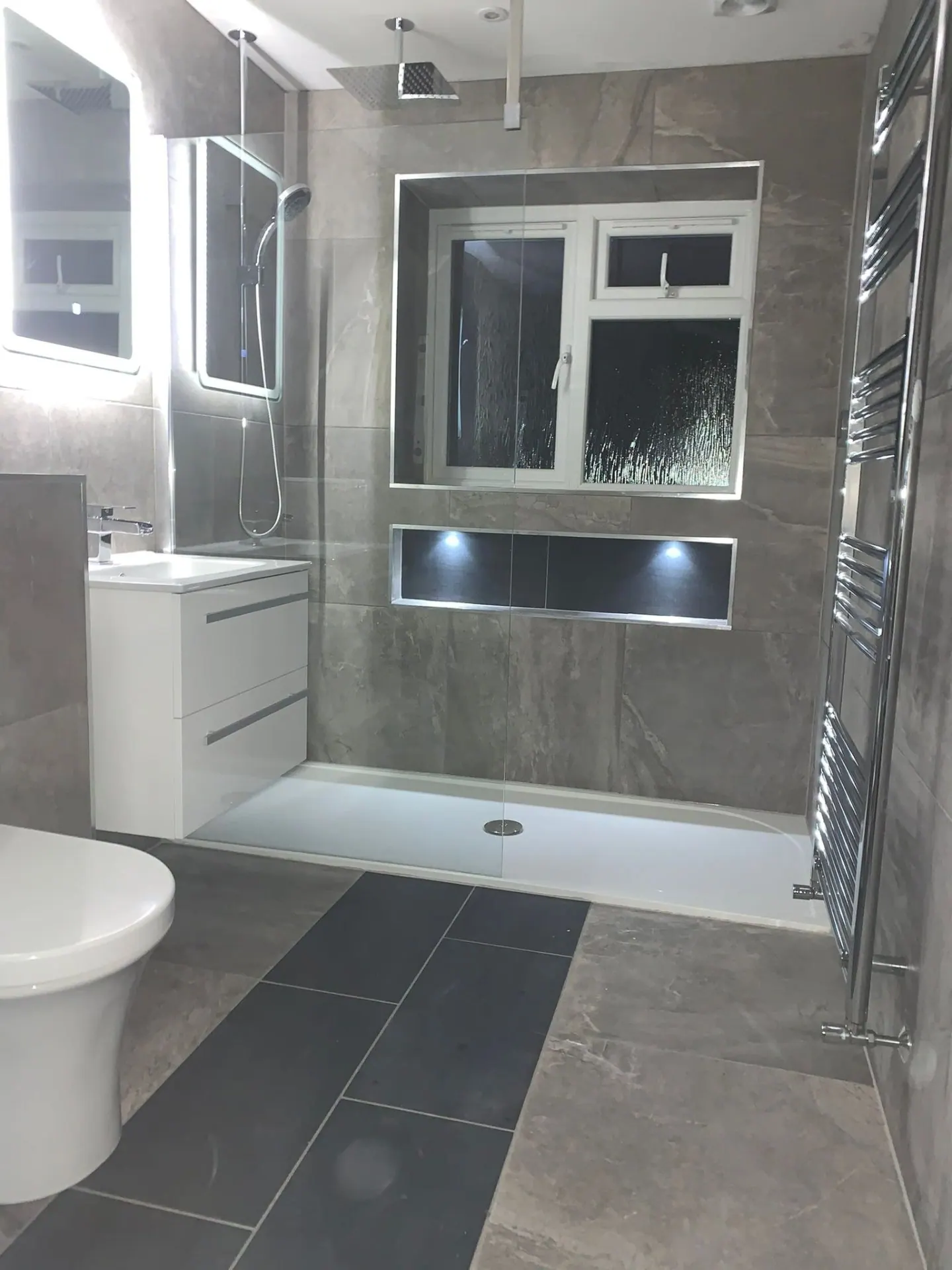 Modern grey-tiled bathroom installation with walk-in shower and heated towel rail in Ashford, Surrey